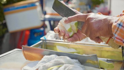 Male hands fast chopping guava on the street market in Thailand.