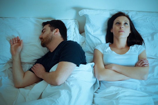 Sad And Thoughtful Woman Awake While Husband Is Sleeping In Bed