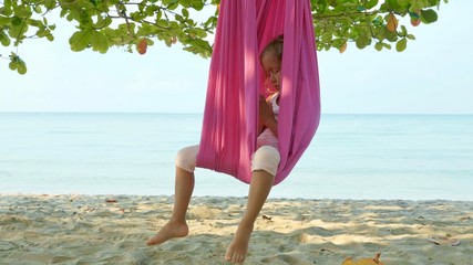 Little cute child girl doing yoga exersice with hammock in the beach.