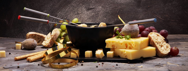 Gourmet Swiss fondue dinner on a winter evening with assorted cheeses on a board alongside a heated...