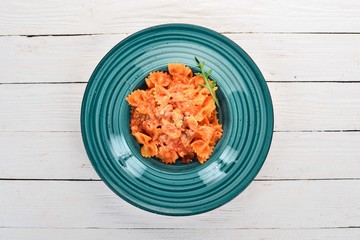 Farfalle pasta with tomatoes and parmesan cheese. On a wooden background. Italian cuisine. Top view. Copy space.