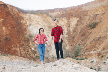 Lovely couple in red plaid shirts standing in sand canyon or quarry with mountain on the background. Outdoor