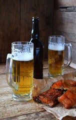 Football fan set with mugs of beer, bottle and salty snacks on wooden background. Junk food for beer or cola. Photographed with natural light. Copy space