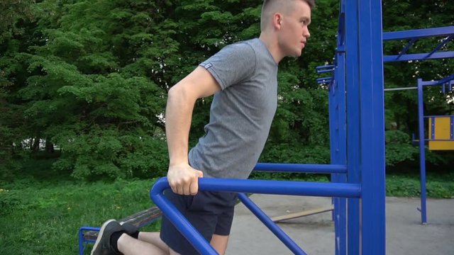 Professional male gymnast training on parallel bars outdoor.