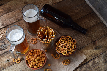 Football fan set with mugs of beer, bottle and salty snacks on wooden background. Junk food for beer or cola. Photographed with natural light. Copy space