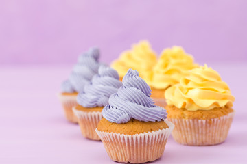 Cupcakes decorated with yellow and violet cream decorations on pastel background.