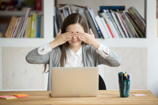 Young female worker covering eyes with hands, making fun during break, playing hide and seek in office. Businesswoman or student working at laptop ignoring seeing something. See no evil concept