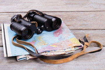 Binoculars and map on wooden table. Top view traveler essentials concept.