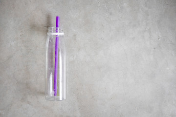 Empty plastic bottle from juice with purple straw on concrete table from above. Ecological, recycling concept. Copy space for text, flat lay
