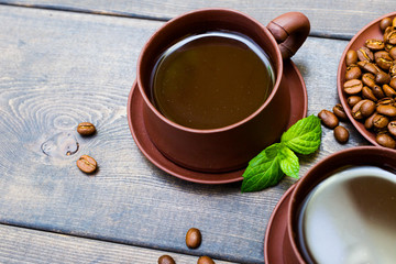 Coffee or chocolate in clay mugs on a background of a wooden table of dark color. A leaf of mint and a grain of coffee.