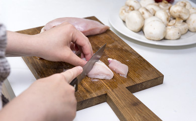Fototapeta na wymiar girl cuts chicken fillet into pieces with a knife