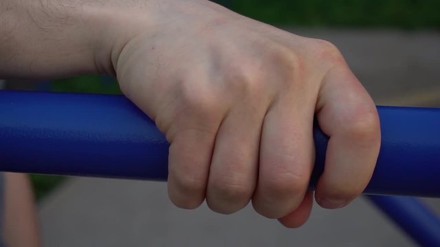 Close up fist of a sportsman doing exercise on parallel bars outdoor.