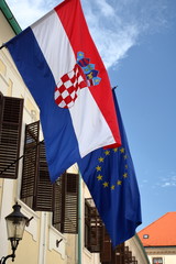 Flaga Chorwacja wisi na ścianie budynku, na zewnątrz, z nią wisi flaga Unii europejskiej, w budynku otwarte okiennice, błękitne niebo w tle - obrazy, fototapety, plakaty