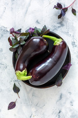 Purple aubergines and basil on a wooden plate. © Saprunova Marina