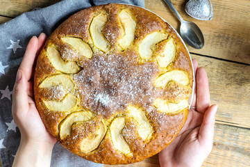 Apple cake on the plate and milk on a wooden table. female hand. Top view