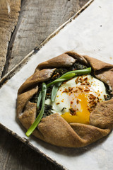 Summer galette with tomatoes, pepper, spinach, feta, cheese, tofu and salt vegetarian dough on wooden desk. Summer food, summer pie on parchment paper, open pie, process of baking