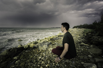 Naklejka na ściany i meble Hombre joven sentado a orillas del mar meditando con el yoga