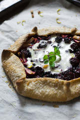 Summer galette with berries, raspberry, blueberry, blackberry, apple and crusty sugar vegetarian dough on wooden background. Summer food, summer pie on parchment paper. Pie with ice cream, sorbet.