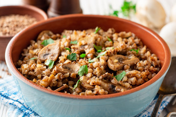 Buckwheat porridge with mushrooms in a bowl on white wooden background