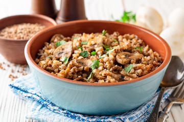 Buckwheat porridge with mushrooms in a bowl on white wooden background