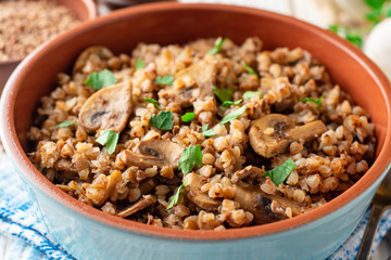 Buckwheat porridge with mushrooms in a bowl on white wooden background