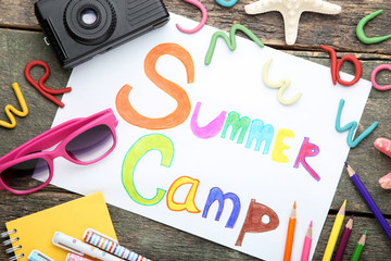 Inscription Summer Camp with sunglasses and retro camera on wooden table