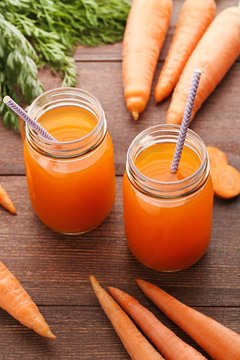 Fresh carrot juice in glass jars on brown wooden background