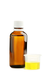 Bottle and measuring plastic cup with medical syrup on white background