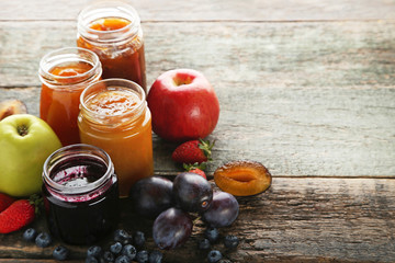 Glass jars with different kinds of jam on wooden table