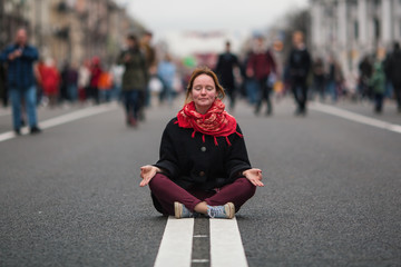 Cute girl sitting in meditation in the middle of a busy street in the city .
