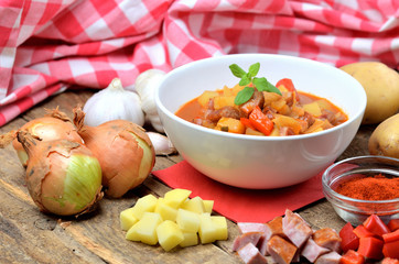 Potato goulash with sausage, pepper, onion and garlic on wooden table