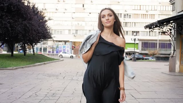 4k footage of stylish young woman in black dress walking on street and looking at camera
