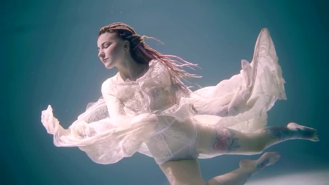 a young woman dressed in a vintage dress posing under the water, a lady moving her hands, she has on her head dreadlocks