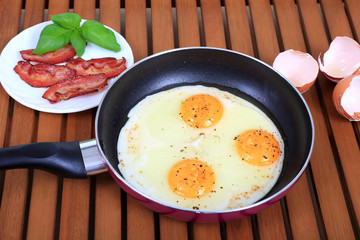 Jajko sadzone na teflonowej patelni z boczkiem i bazylą i skorupkami w tle. © Stanisław Błachowicz