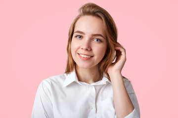 Obraz premium Lovely cute female with positive smile, wears white elegant shirt and stylish cap, going to school or college in good mood, isolated over studio background. Hipster girl spends time with friends
