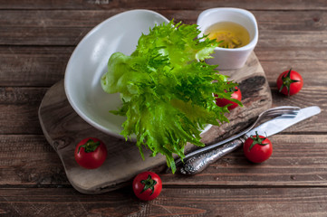 Fresh green lettuce in a plate and olive oil with spices on a wooden background. Top view