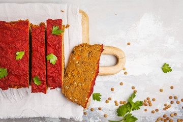 Vegetarian lentil casserole (sliced) with vegetables and tomato sauce on a wooden board, top view, copy space. Healthy vegan food concept.