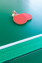 Plakat View of two red table tennis bats or rackets with a white ball on a green table with a net