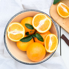 Juicy and fresh oranges with leaves  in bowl on white wooden table. Eye bird view 