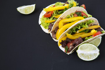 Tacos with beef and vegetables and lime on a black background, side view. Closeup.