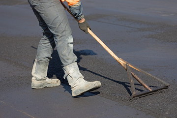 Construction road worker levelling hot mix flexible asphalt concrete pavement