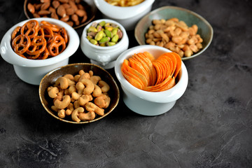 Different kinds of snacks - chips, salted peanuts, cashews, almonds and pistachios, pretzels with salt, potatoes, salted straw.