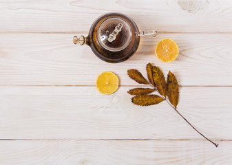 glass teapot with tea,lemon and leaves.white wooden background.top view.space for text