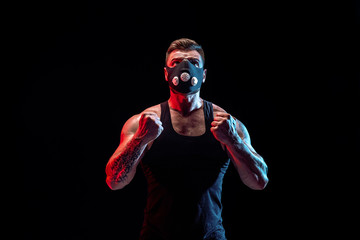 Strong male athlete in a black training mask posing on a black background