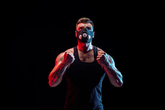 Strong Male Athlete In A Black Training Mask Posing On A Black Background