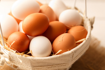 Fresh brown and white chicken eggs in a basket on light wooden table
