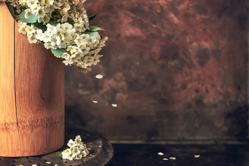Japanese philosophy Wabi Sabi background. White small flowers spirea with falling petals in a brown wooden vase on vintage rusty background - obrazy, fototapety, plakaty