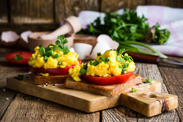 Scrambled eggs on two pieces of toast with green onion and tomatoes