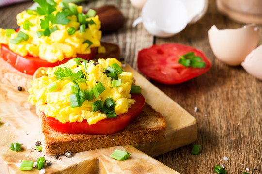 Scrambled eggs on two pieces of toast with green onion and tomatoes