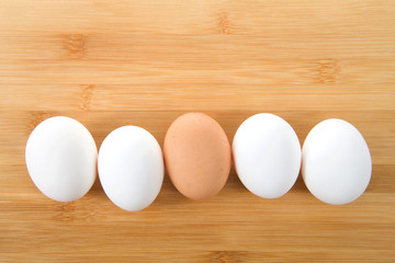 Row of eggs, one brown four white on a light wood table. Diversity concept.